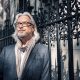 Editorial portrait of a silver-haired man in glasses beside iron railings in London